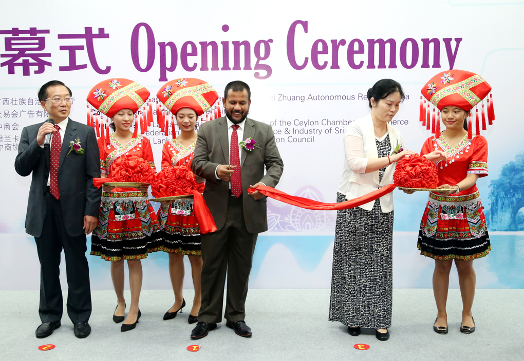 Minister of Industry and Commerce of Sri Lanka Rishad Bathiudeen (centre) splits the red ribbon at the traditional Chinese ribbon cutting ceremony on 14 July in Colombo to launch the first ever product exhibition in Sri Lanka by China's Guangxi Zuang Autonomous Region joined by visiting Deputy DG of Department of Commerce of Guangxi Xiong Jiajun (left), Charge d'affairs of Chinese Embassy in Sri Lanka Ms Pang Xunshie (right) and Zhuang traditional garb attired Chinese women